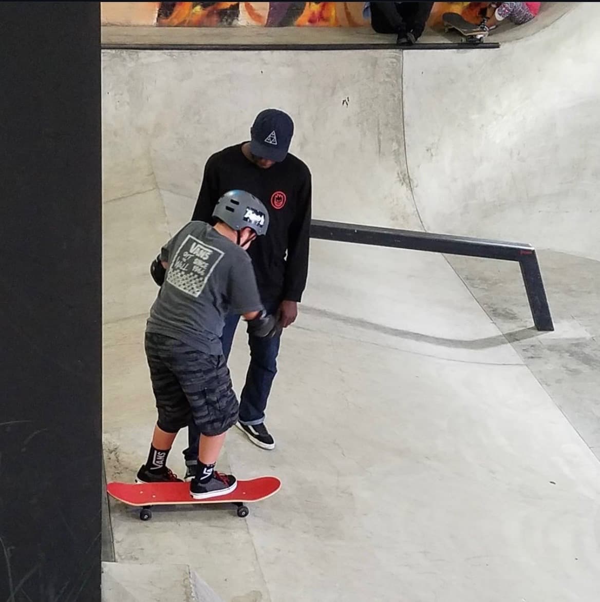 Leon Toppin teaching a kid at an indoor skatepark