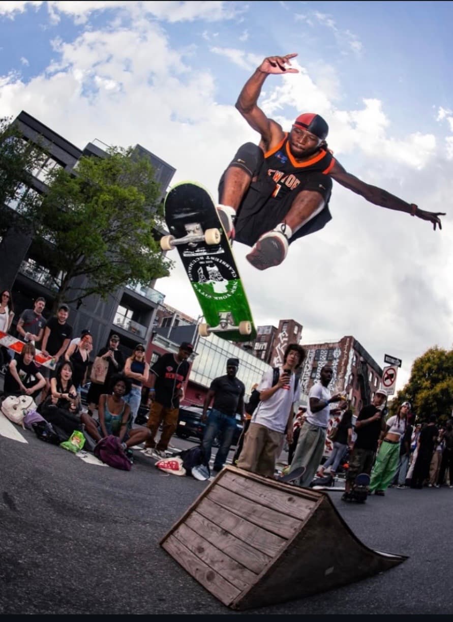 Leon Toppin performing a kickflip over a ramp in front of a large crowd